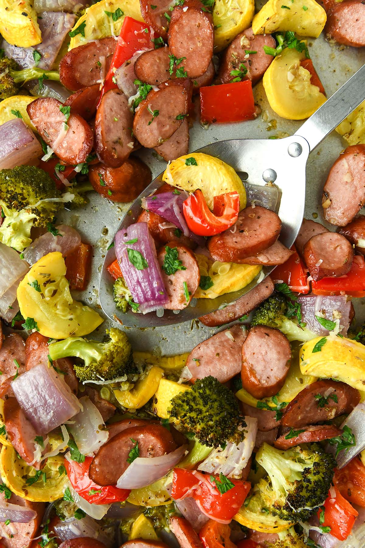 Up close and above view of baked vegetables on a sheet pan with a serving spoon.