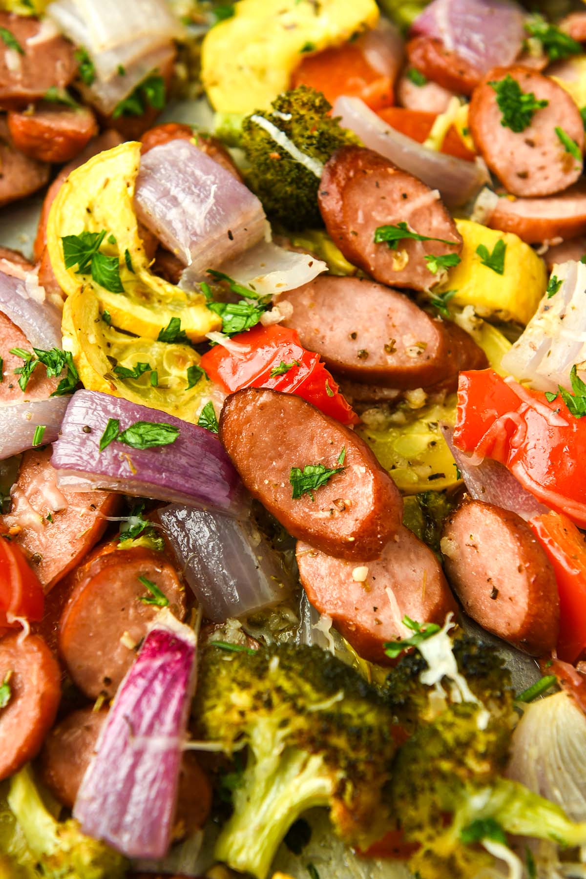Up close of baked vegetables on a sheet pan with a serving spoon.