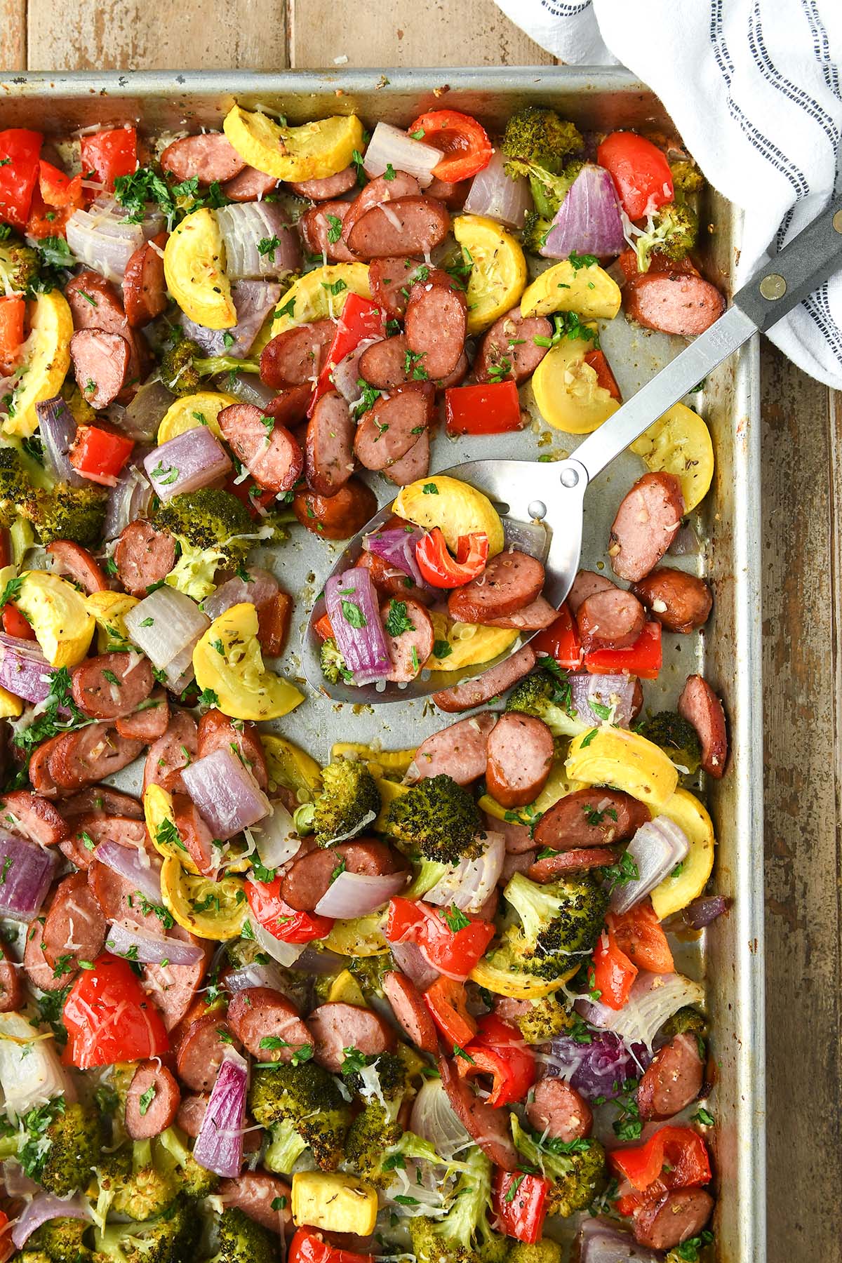 Above view of baked vegetables on a sheet pan with a serving spoon.