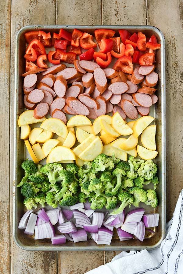 Step one is adding all of the vegetables and sliced sausage to the sheet pan.