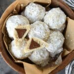 Above view of a wooden bowl full of snowball cookies with one cut open so you can see the chocolate kiss inside.
