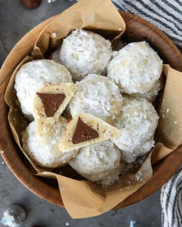 Above view of a wooden bowl full of snowball cookies with one cut open so you can see the chocolate kiss inside.