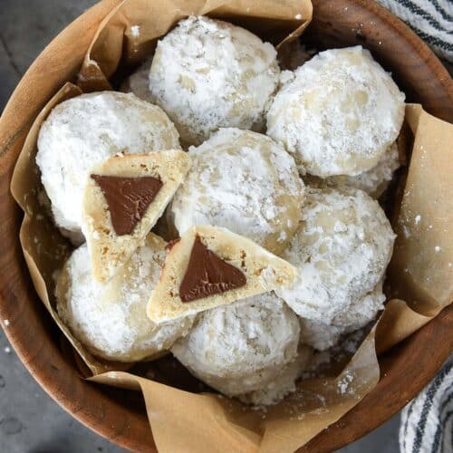 Above view of a wooden bowl full of snowball cookies with one cut open so you can see the chocolate kiss inside.