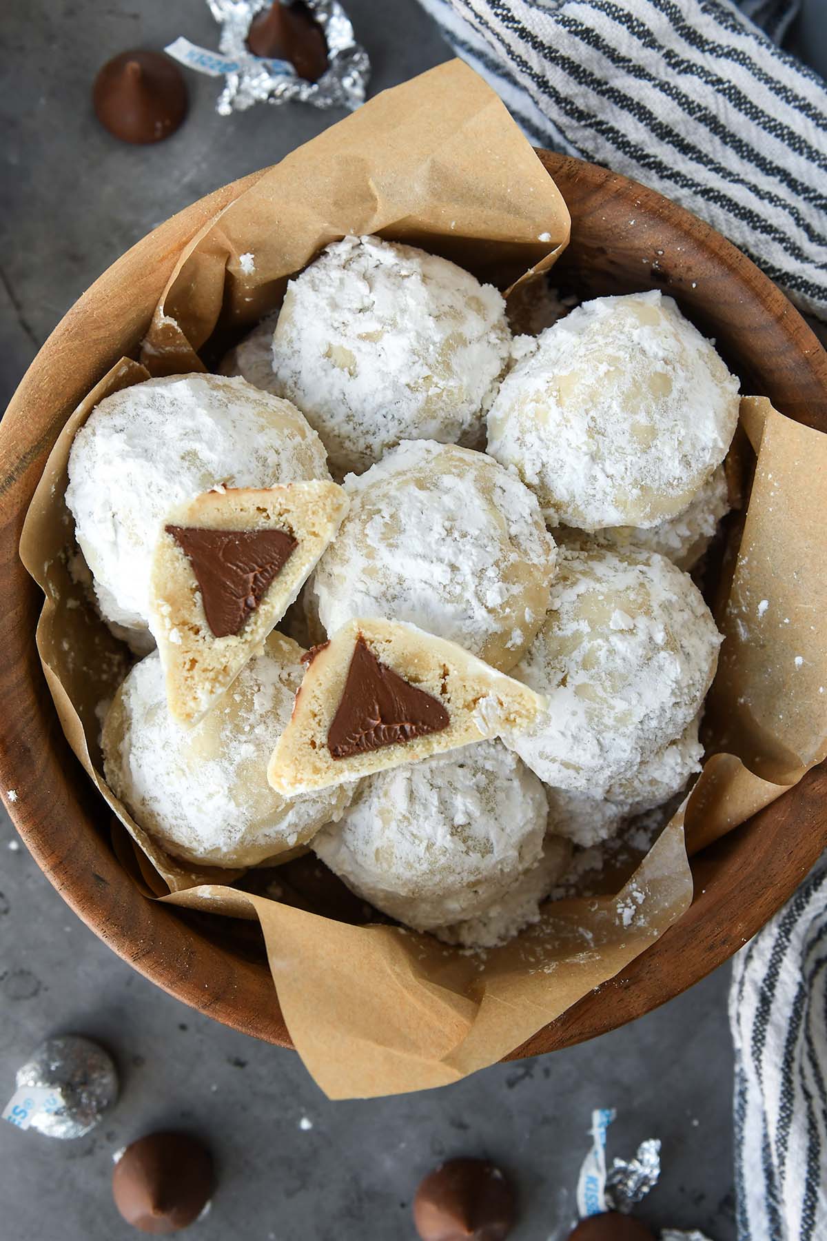 Above view of a wooden bowl full of snowball cookies with one cut open so you can see the chocolate kiss inside.