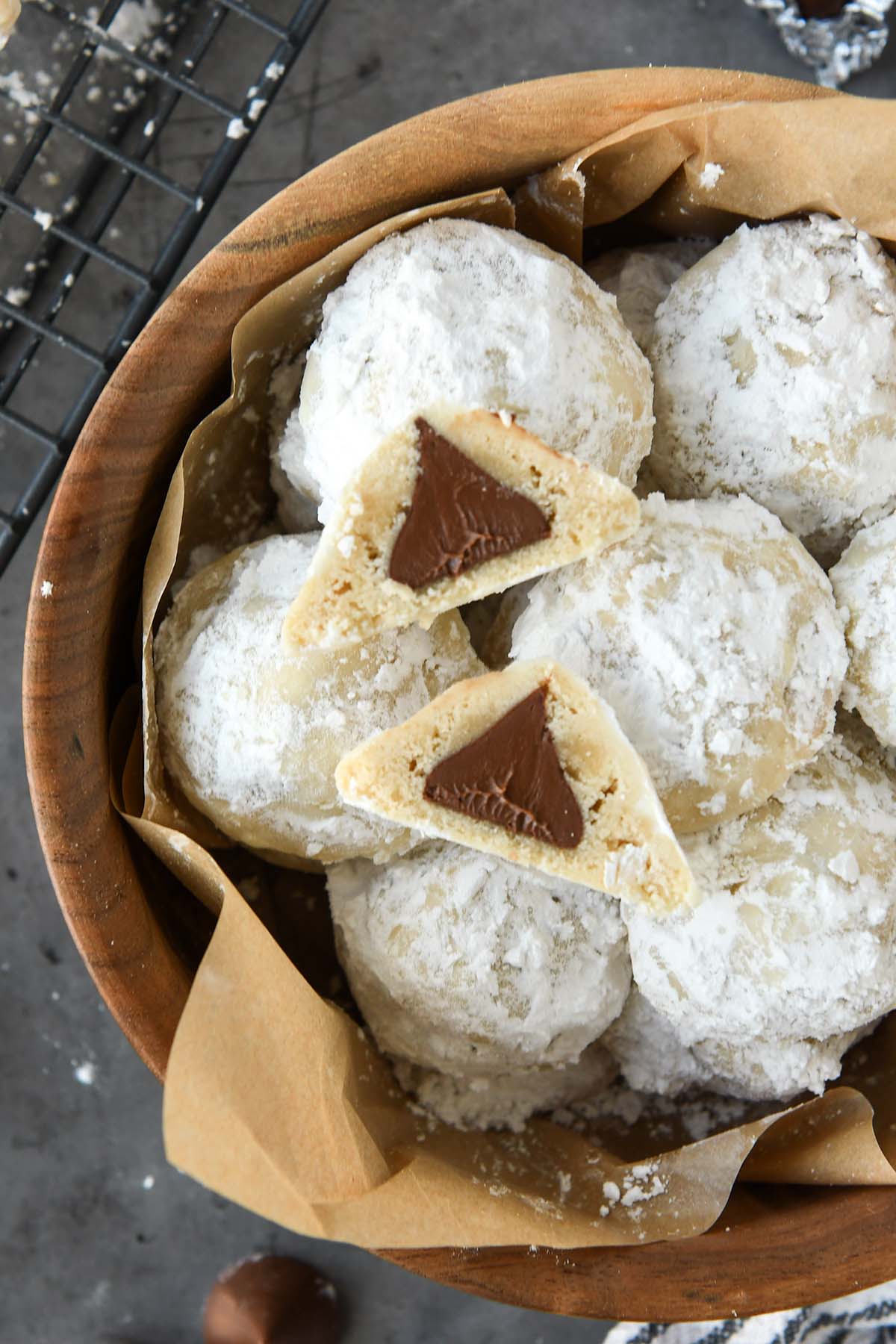 Above view of a wooden bowl full of snowball cookies with one cut open so you can see the chocolate kiss inside.