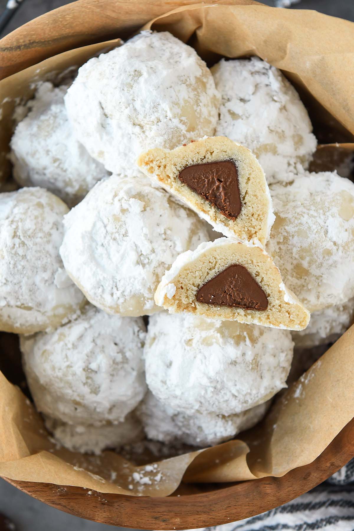 Super close up of an above view of a wooden bowl full of snowball cookies with one cut open so you can see the chocolate kiss inside.