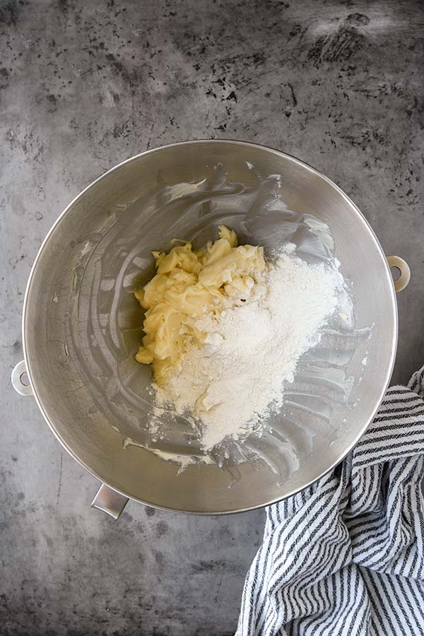 Step two is The mixing bowl has been scraped down after mixing together the butter and powdered sugar. The flour is added.