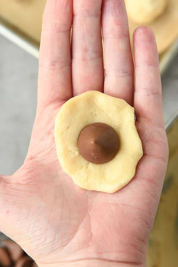 Step four is flattening a tablespoon sized scoop of dough. Then place a Hershey kiss in the center and wrap the dough around it.