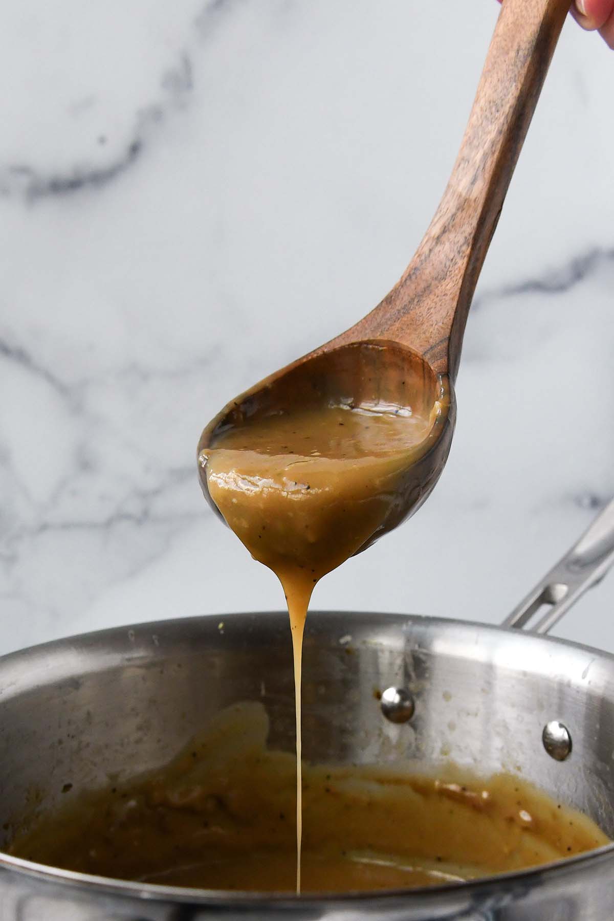 A ladle of gravy being lifted out of a cooking pot.