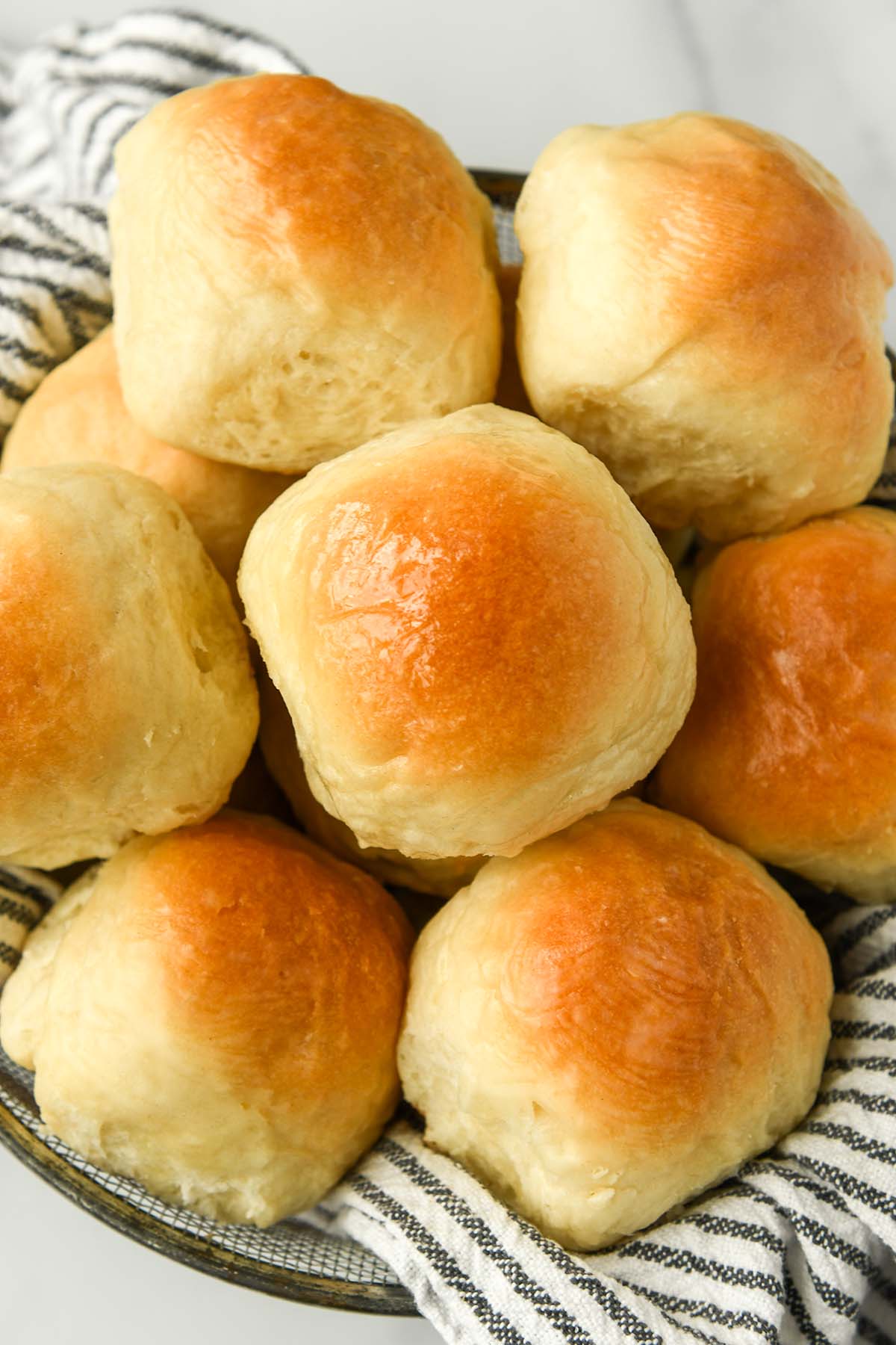 Above view of dinner rolls in a basket with a striped towel.