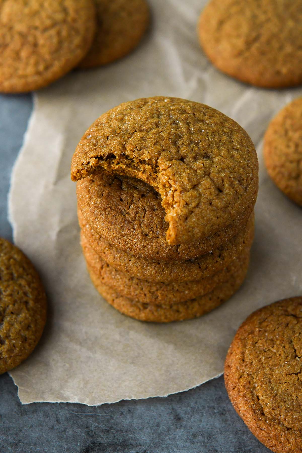 A stack of molasses cookies with the one of top missing a bite and some more cookies all around the stack.