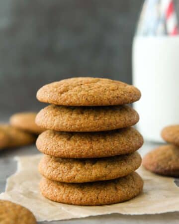 Front view of a stack of five molasses cookies with a glass of milk.