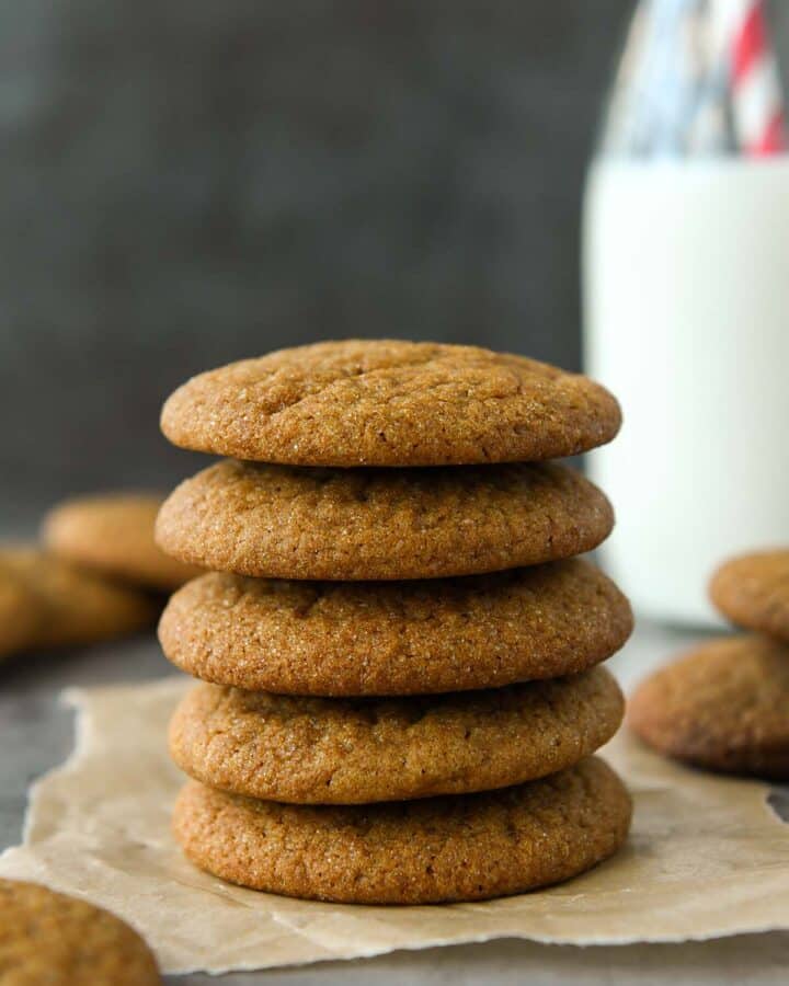 Front view of a stack of five molasses cookies with a glass of milk.