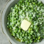 An above view of a bowl of creamed peas with a melty pat of butter and a white and black striped towel.