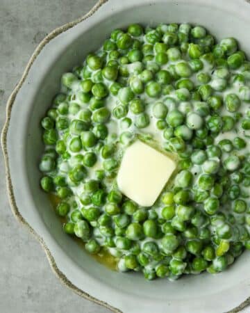 An above view of a bowl of creamed peas with a melty pat of butter and a white and black striped towel.