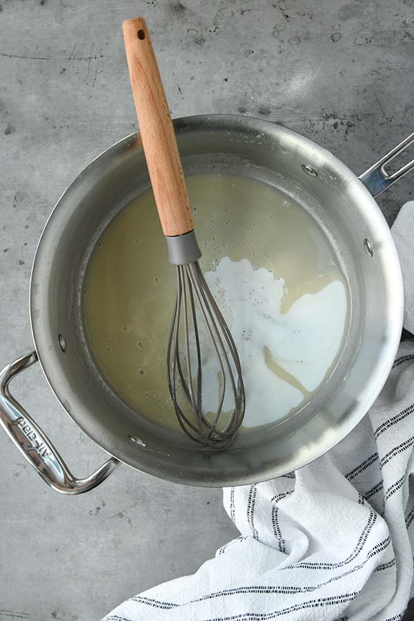 Step two is half and half being mixed into the roux with a whisk in a pan.