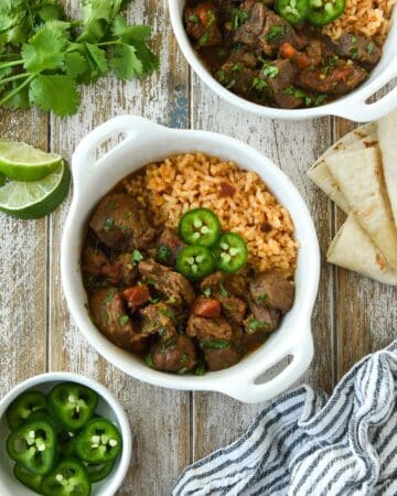 Two bowls of carne guisada served on Mexican rice and topped with slices of jalapeno.