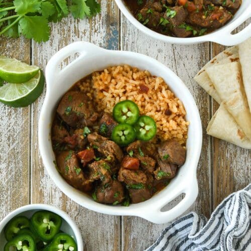 Two bowls of carne guisada served on Mexican rice and topped with slices of jalapeno.