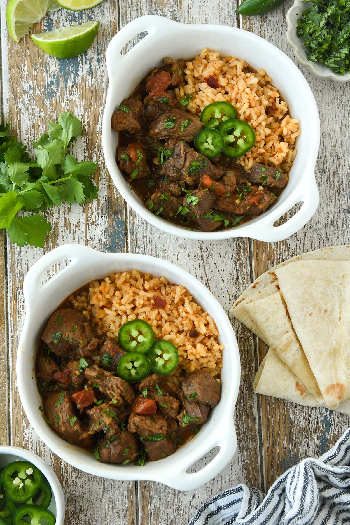 Above view of two bowls of carne guisada served on Mexican rice and topped with slices of jalapeno. 