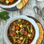 Above view of two bowls of hamburger soup with ritz crackers and spoons.