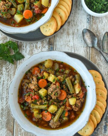 Above view of two bowls of hamburger soup with ritz crackers and spoons.