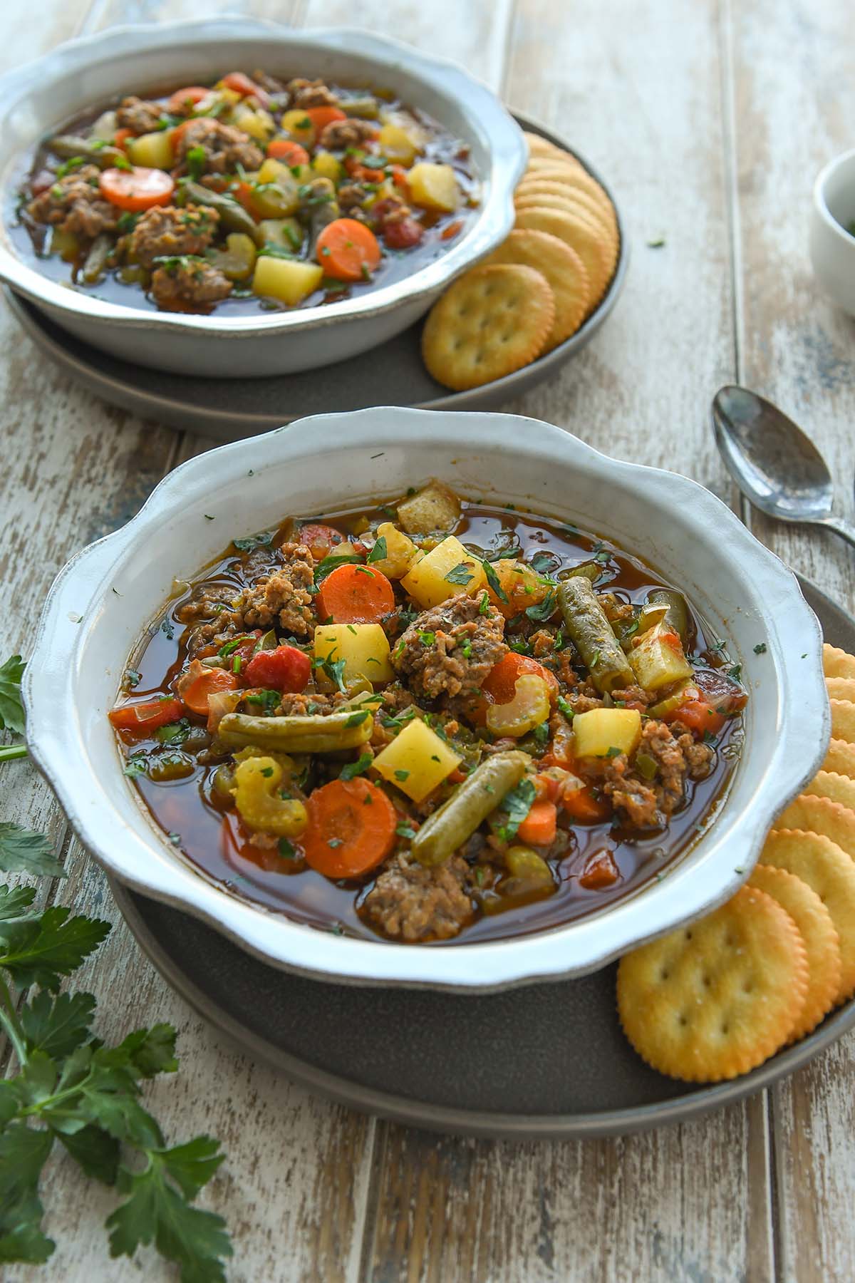 Two bowls of hamburger soup with ritz crackers and spoons.
