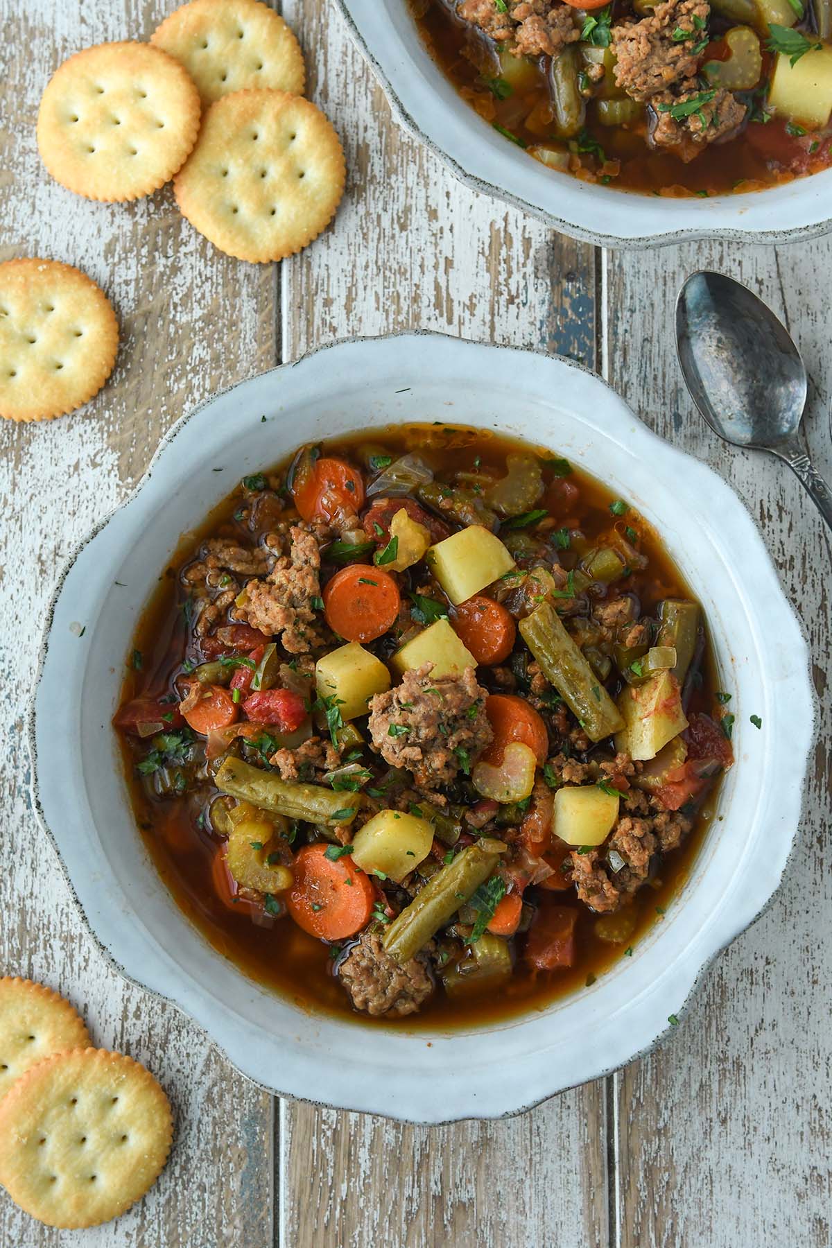 Above view of two bowls of hamburger soup with ritz crackers and spoons.