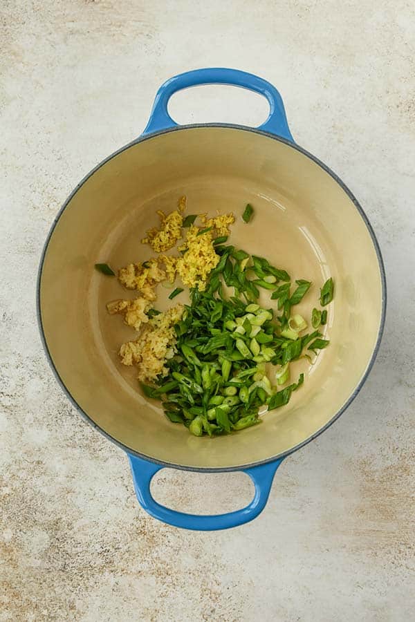 Step one is adding the sliced green onions, ginger, and garlic to the pot.