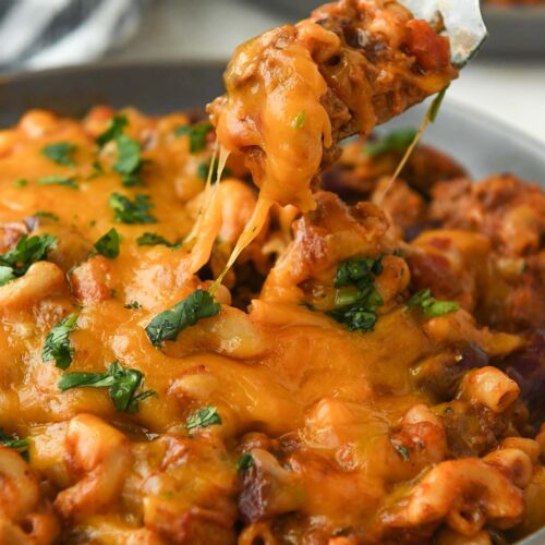 A forkful of chili mac above a plate with gooey cheese.