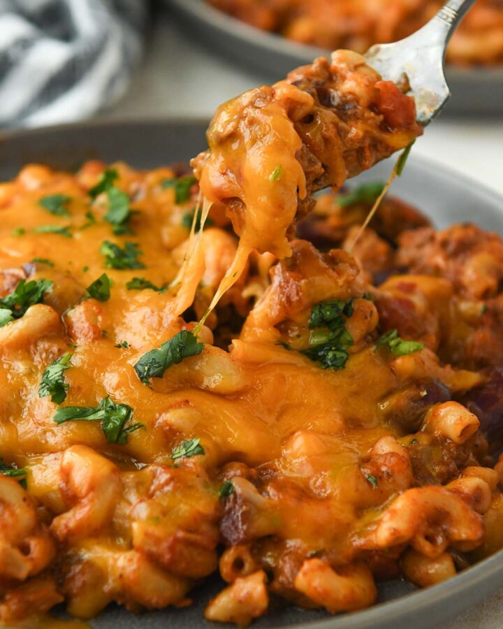 A forkful of chili mac above a plate with gooey cheese.