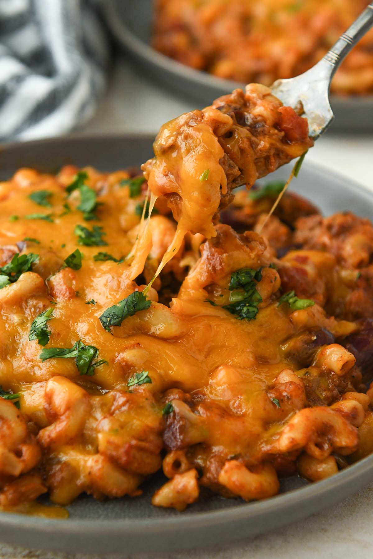 A forkful of chili mac above a plate with gooey cheese.