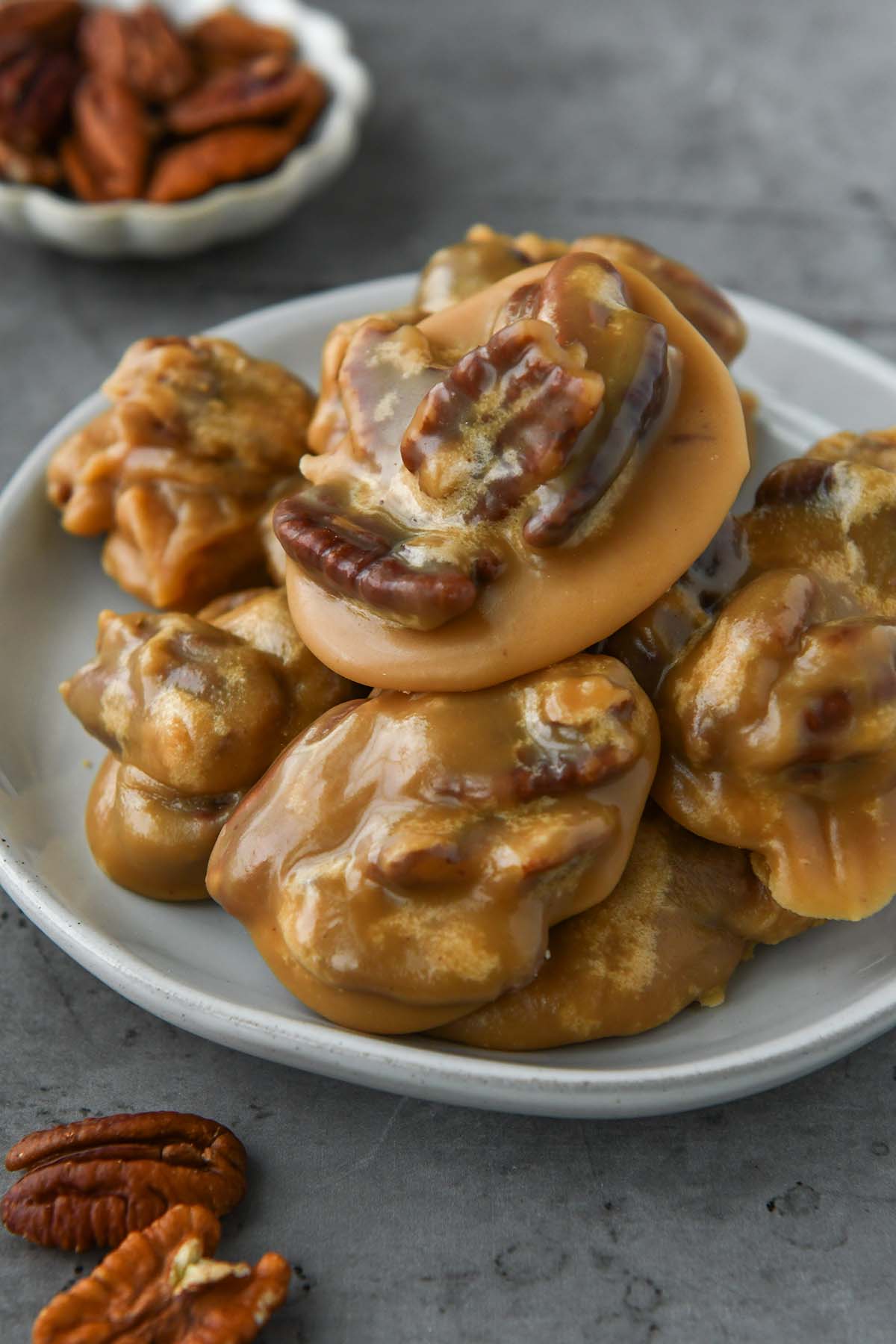 Above view of pecan pralines on a plate with some extra pecans around.