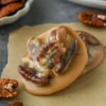 Up close of a new orleans pecan pralines on a piece of parchment with some extra pecans around and a plate of pralines.