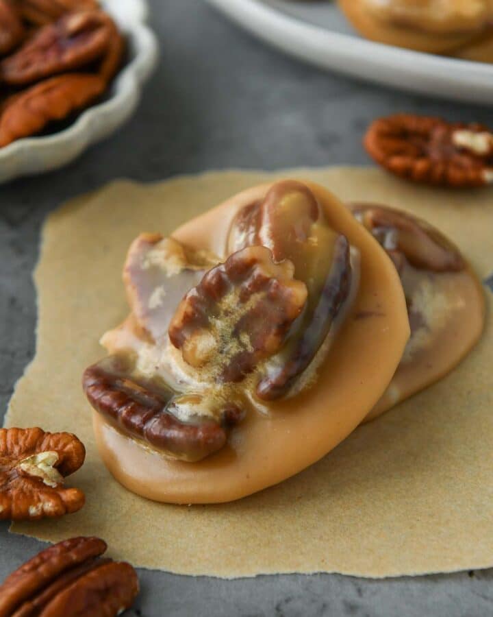 Up close of a new orleans pecan pralines on a piece of parchment with some extra pecans around and a plate of pralines.