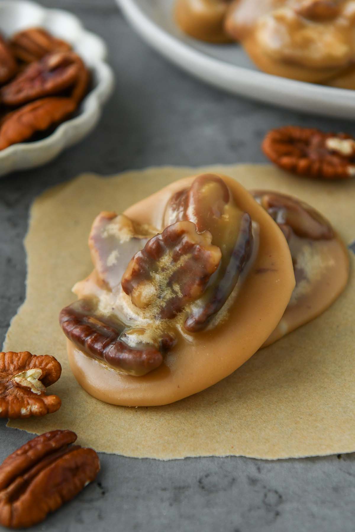 Up close of a new orleans pecan pralines on a piece of parchment with some extra pecans around and a plate of pralines.