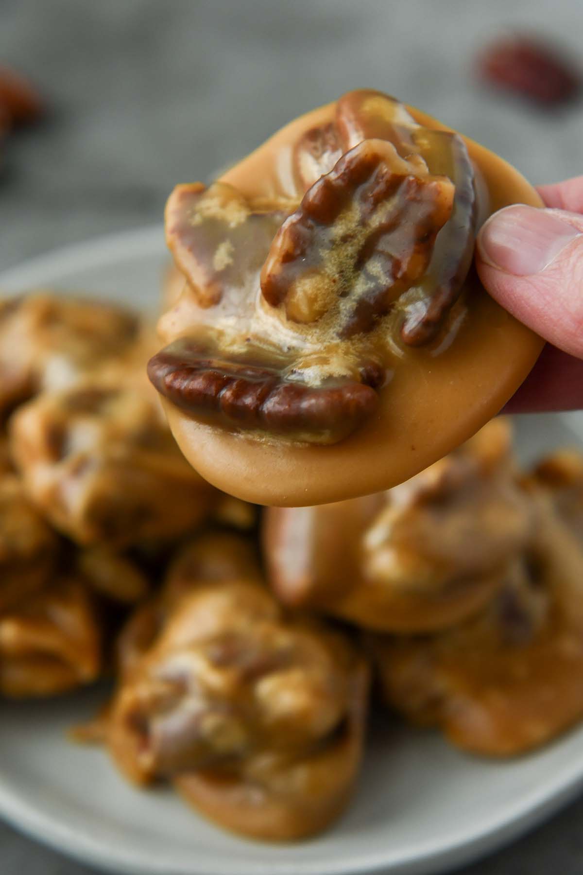 Up close of a new orleans pecan pralines being held above a plate of pralines.