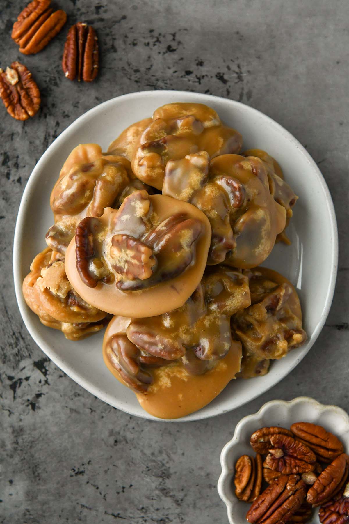 Above view of pecan pralines on a plate with some extra pecans around.