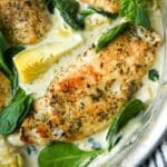 Up close above view of spinach artichoke chicken in a pan with a striped towel.