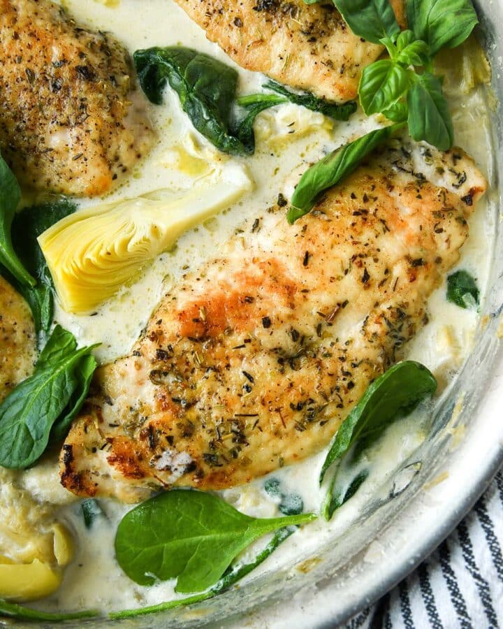 Up close above view of spinach artichoke chicken in a pan with a striped towel.