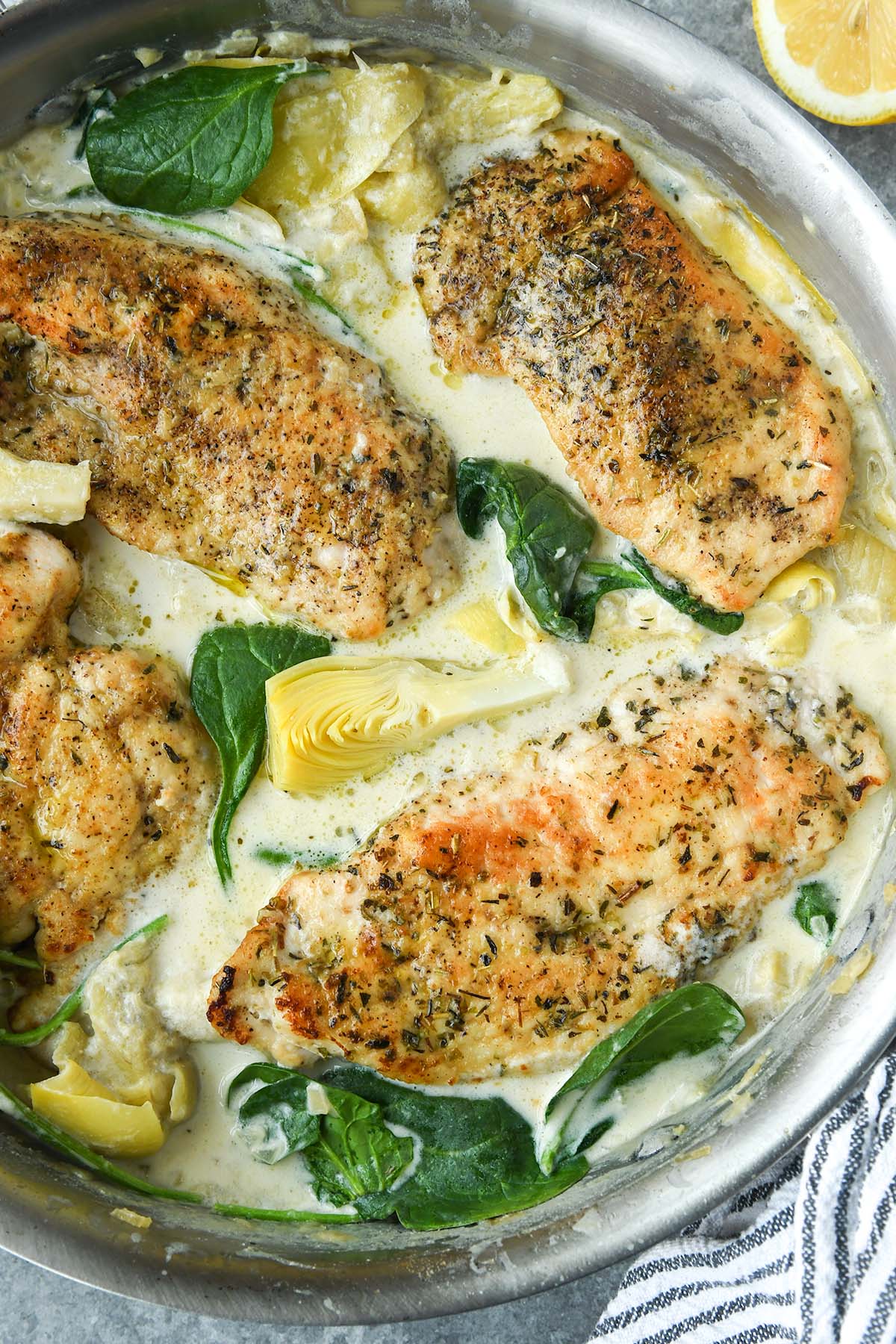 Up close above view of spinach artichoke chicken in a pan with a striped towel.