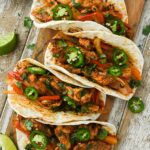 Above view of four fajitas in tortillas topped with jalapenos and a side of sour cream.