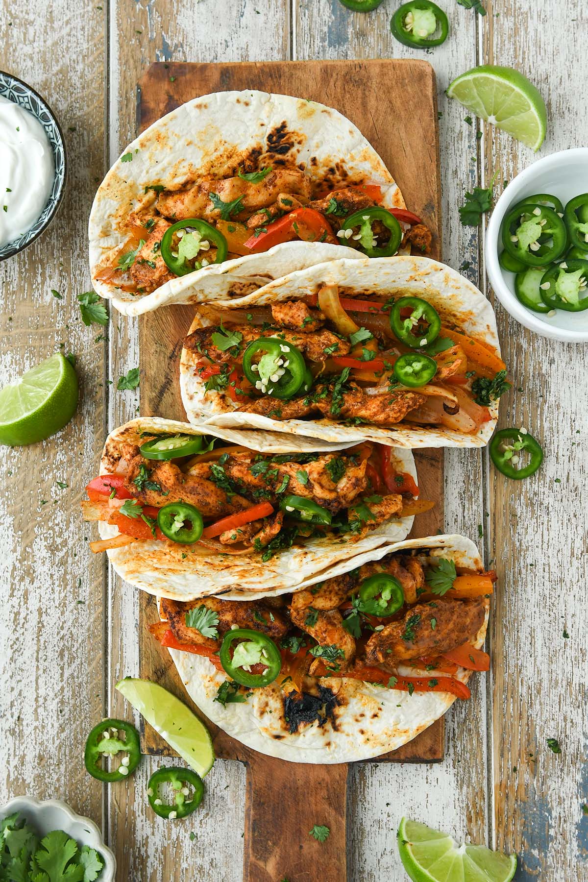 Above view of four fajitas in tortillas topped with jalapenos and a side of sour cream.