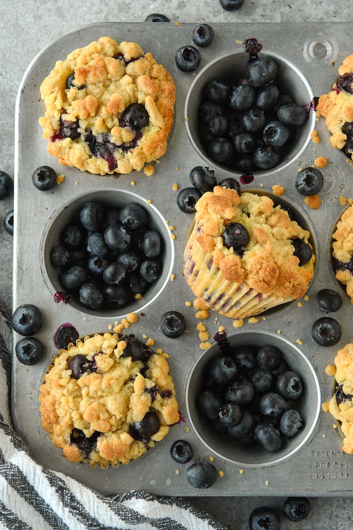 Above view of a muffin tin with three muffin holes filled with fresh blueberries and the other three filled with blueberry muffins.