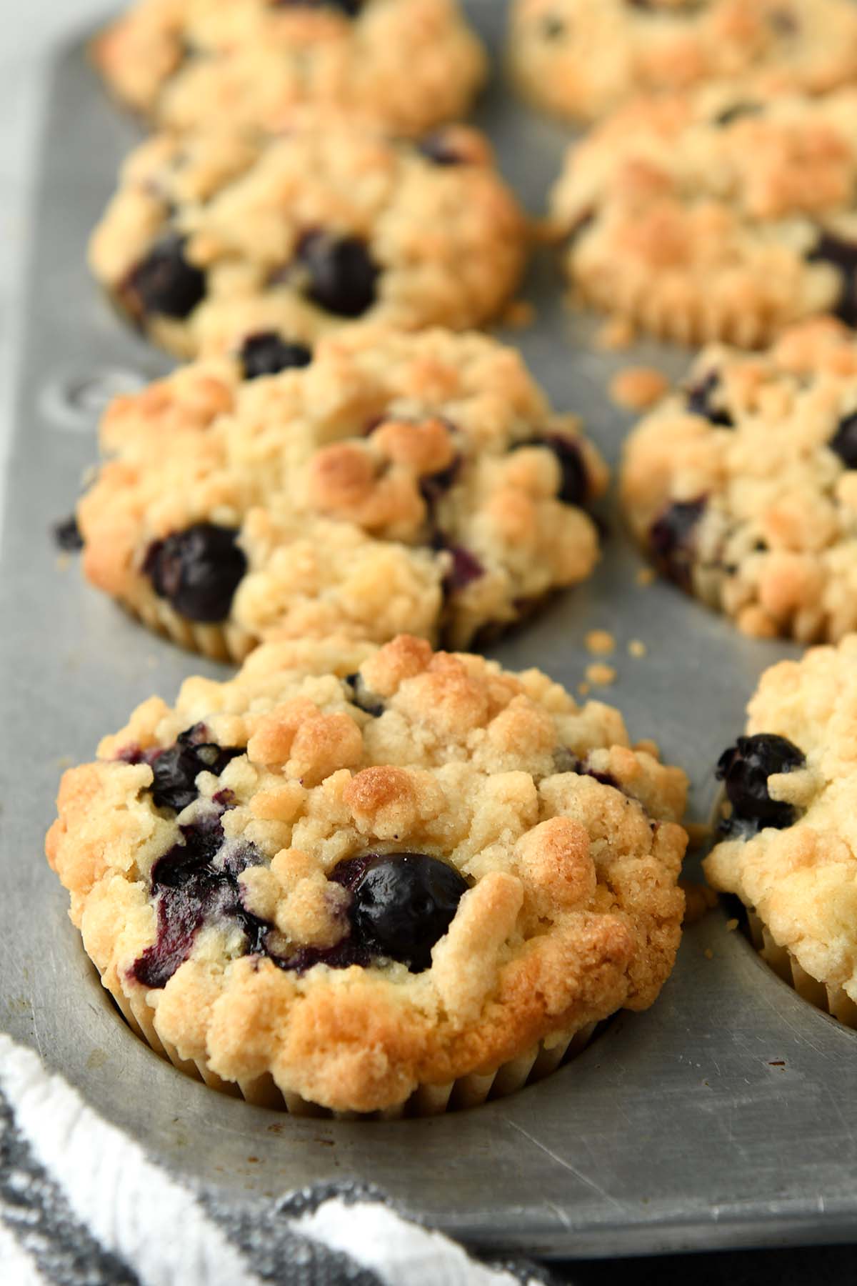 Up close of a blueberry muffins in the muffin tin with a striped towel.