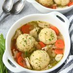 Above view of matzo ball soup with chicken and vegetables, a striped towell and spoons.