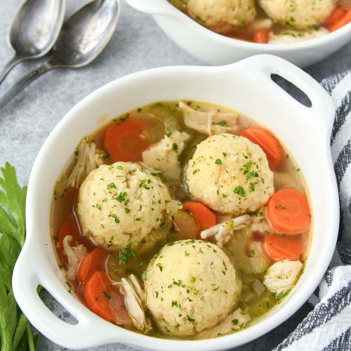 Above view of matzo ball soup with chicken and vegetables, a striped towell and spoons.