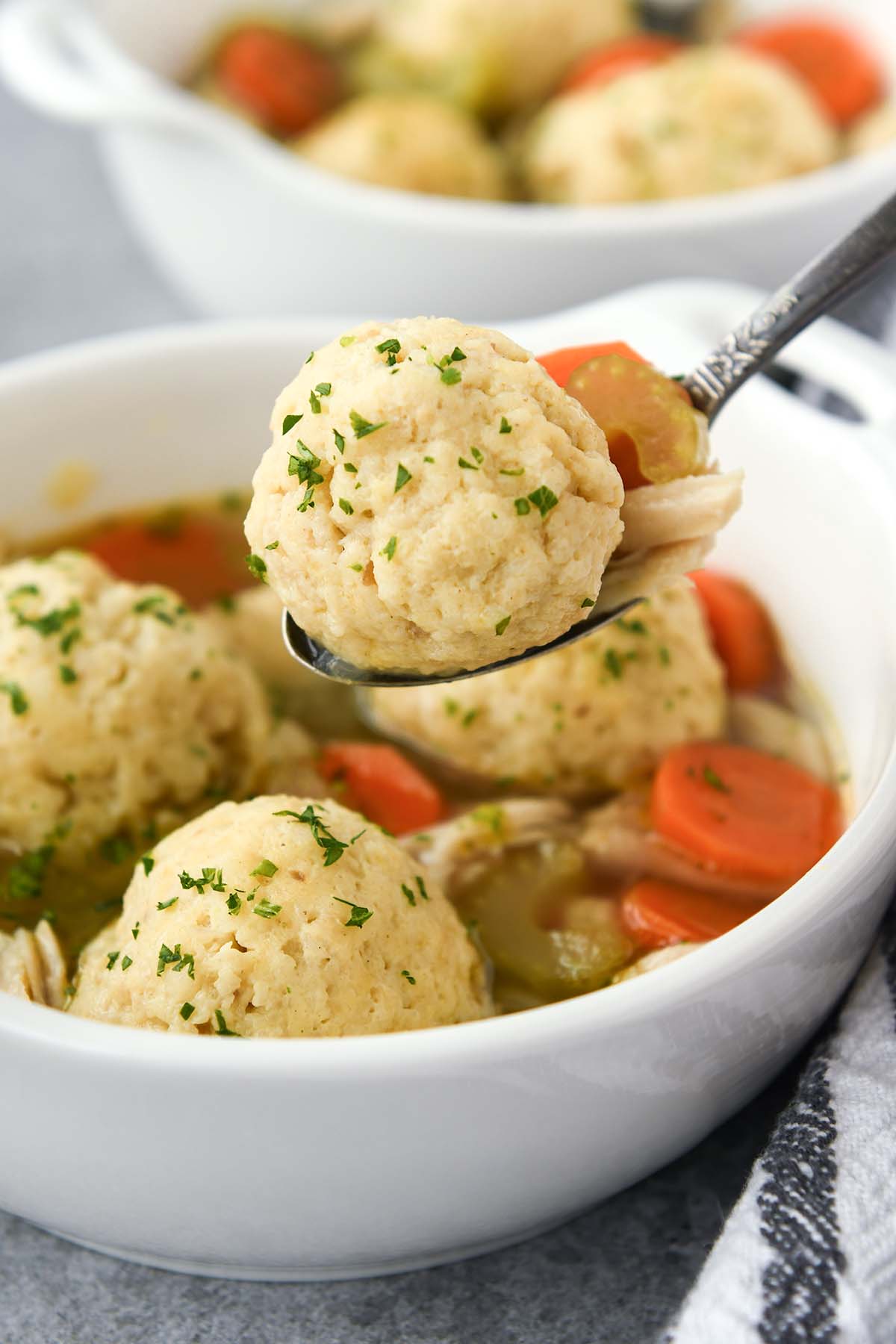 A matzo ball on a spoon above a whole bowl of matzo ball soup.