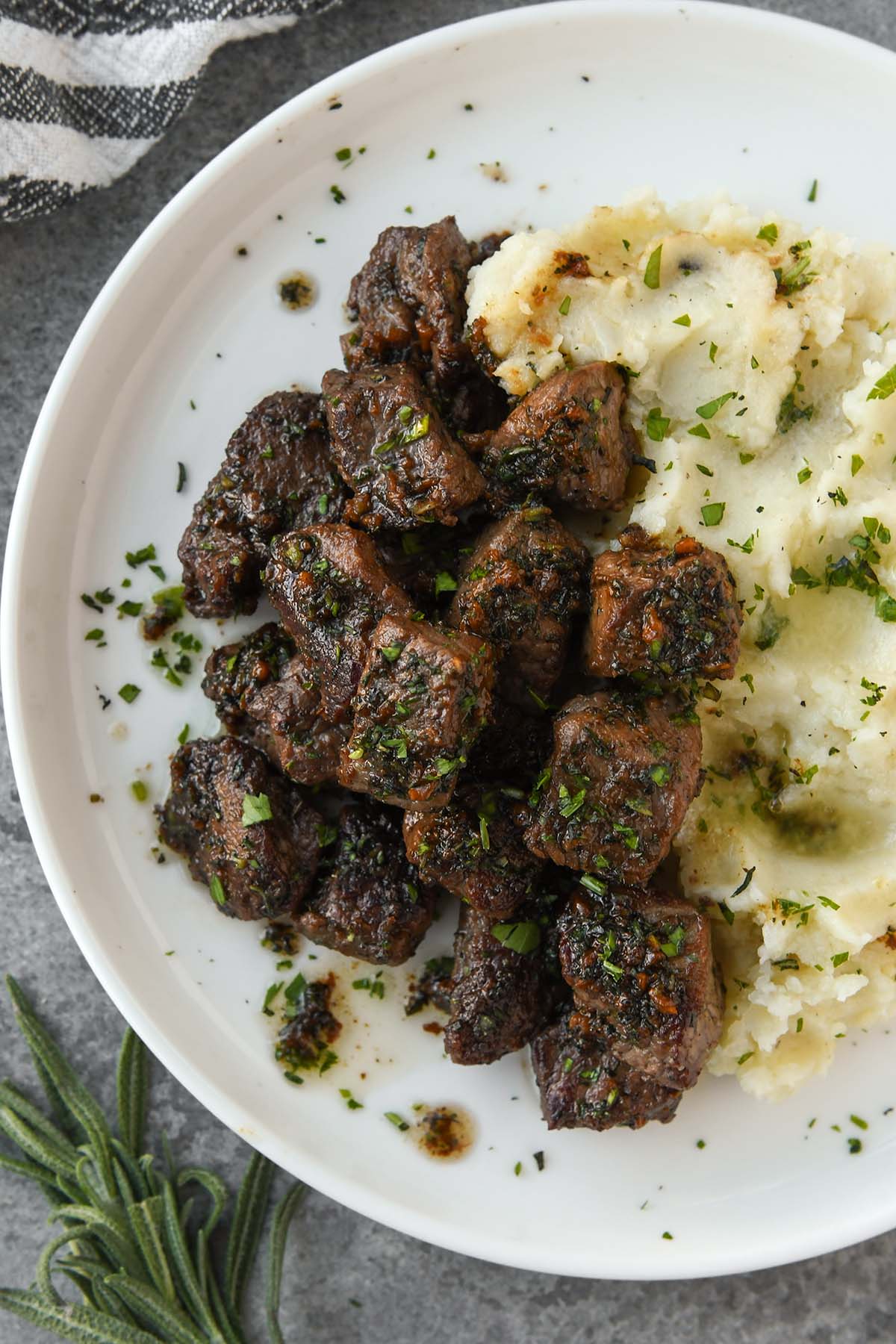 Above view of a plate of garlic steak bites sprinkled with chopped parsley with mashed potatoes.