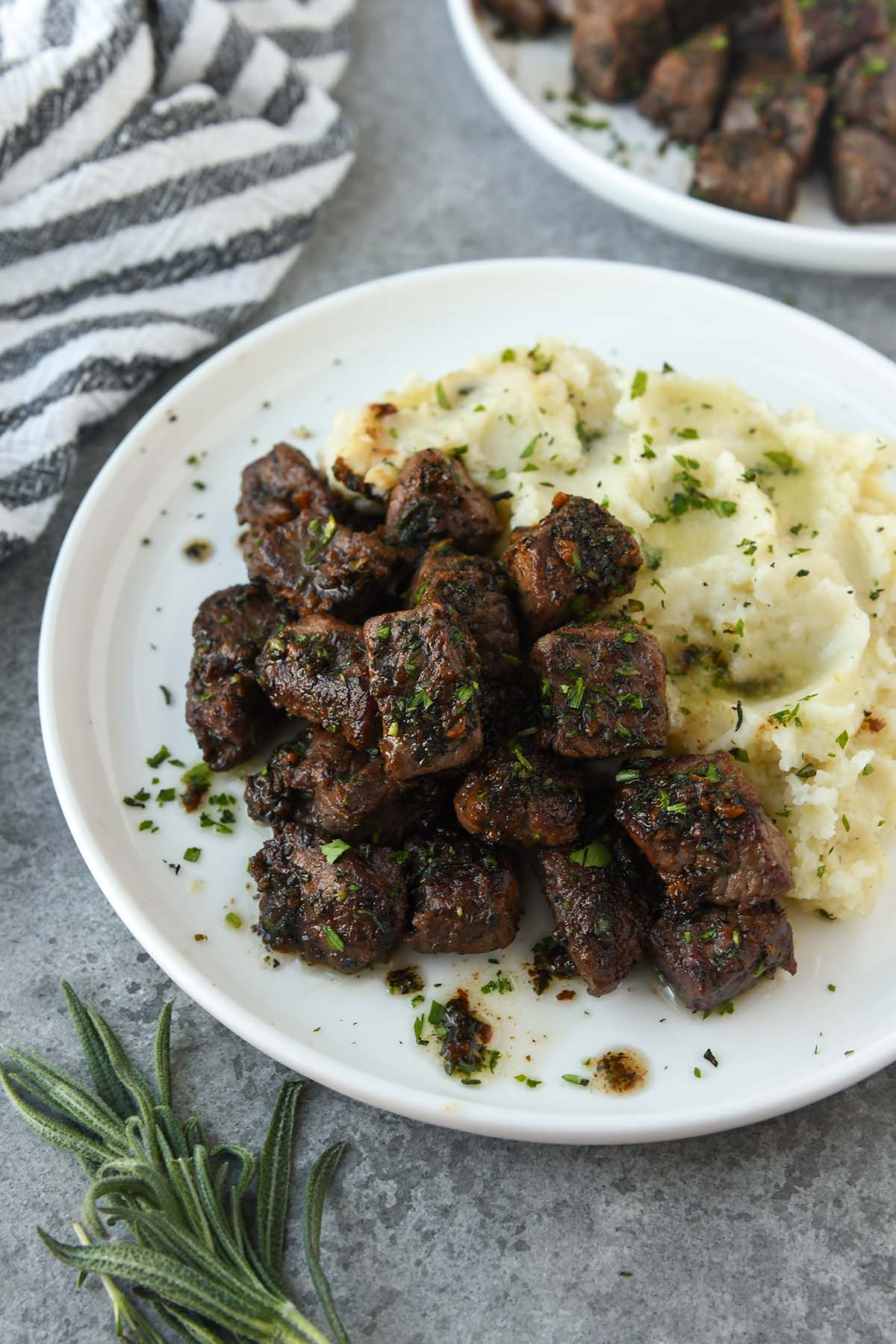 A plate of garlic steak bites sprinkled with chopped parsley with mashed potatoes.