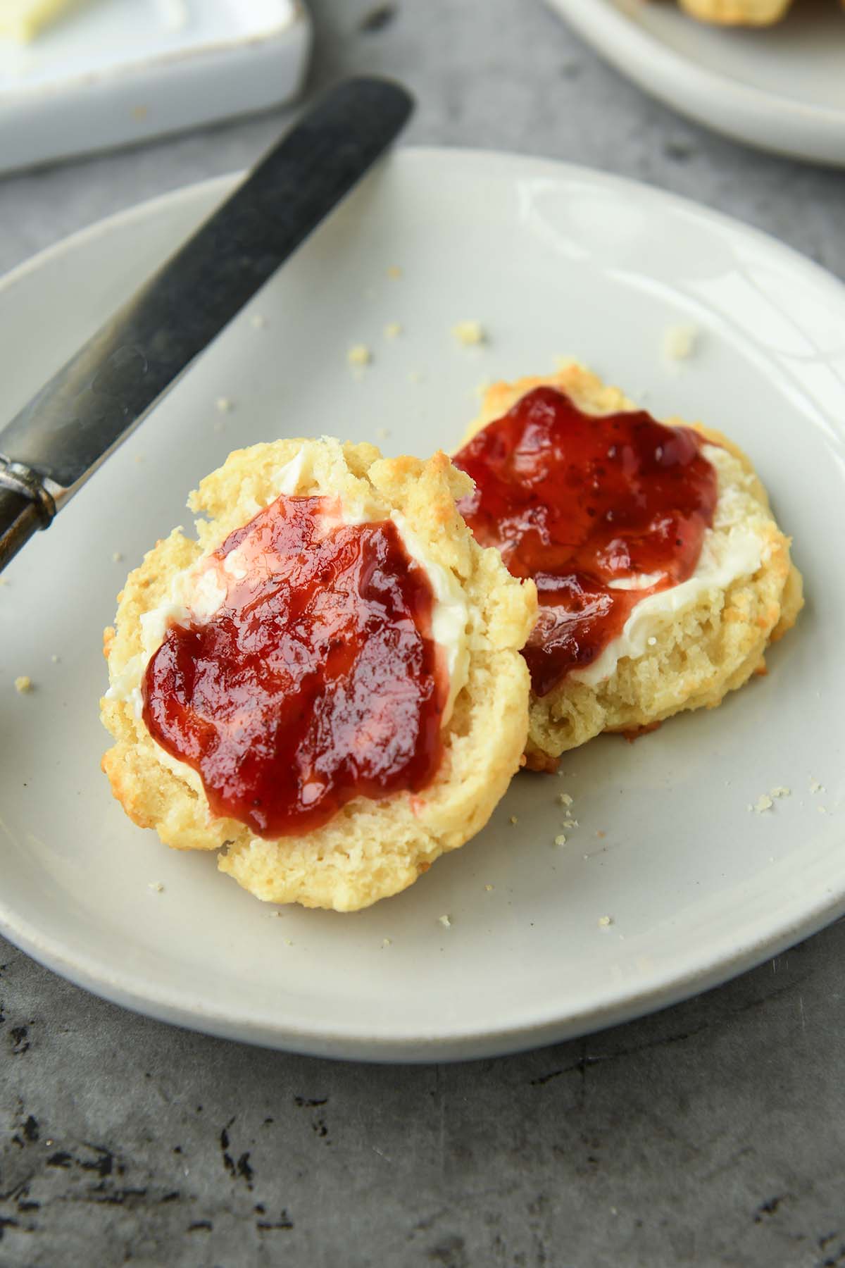 Up close of a biscuit slathered with butter and jelly on a plate with a knife. 